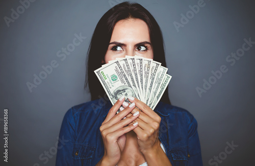 You can make purchases. Beautiful young woman in casual clothes joyfully holding in her hand a lot of dollars on a gray background isolated. The concept of money and banking.