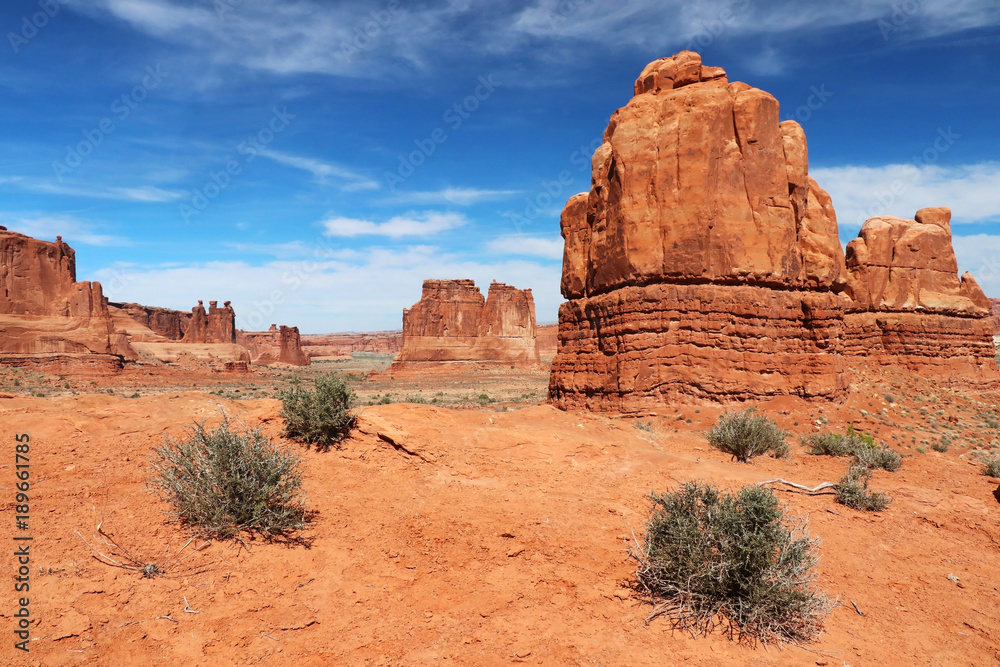 Amazing Utah landscape with red sandstones in Arches National Park, Moab, Utah, USA. Nature red sandstone sculptures with sparse green bushes on a foreground against bright blue sky. Travel America.
