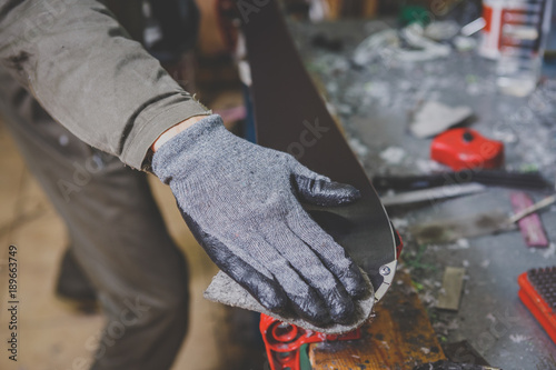 A man in work clothes repairman in a workshop ski service repairing the sliding surface of skis. In the hands of a tool, Final polishing. Theme ski repair and maintenance of equipment