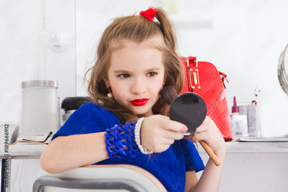beautiful little girl in the mirror preening and using makeup to imitate adults. Child cosmetics. 