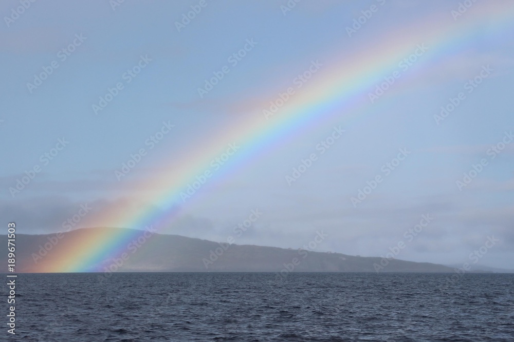 Regenbogen am Meer mit Hügeln im Hintergrund Regenbogen am Meer mit Hügeln im Hintergrund