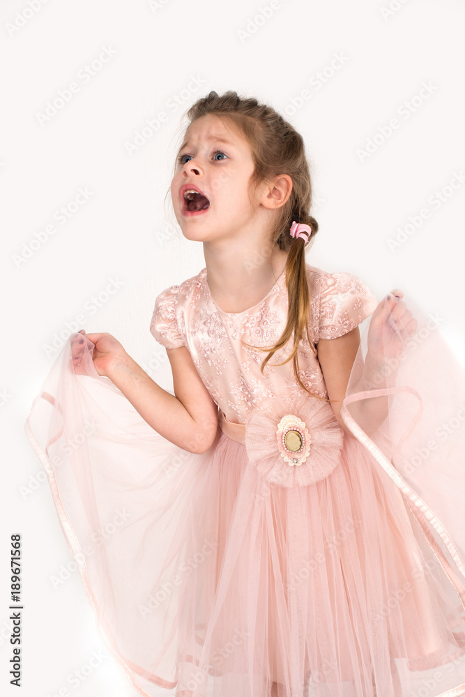 The girl in a pink ball dress and with blue eyes stands at a wall. She is capricious; The girl in a pink ball dress and with blue eyes stands at a wall. She is capricious;