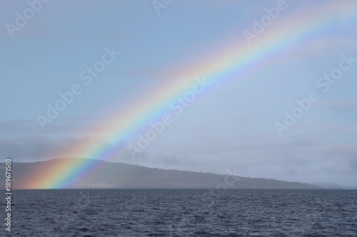 Regenbogen am Meer mit H  geln im Hintergrund