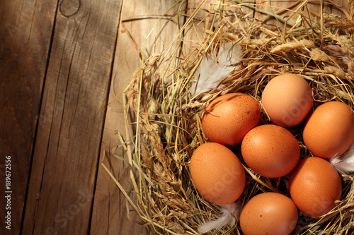 Hen organic eggs in the nest. On wooden rustic background.Copy space.Top view