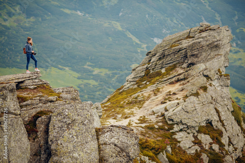 Shot of a young woman taking pictures from the top of a mountain. Hiker standing on a rock