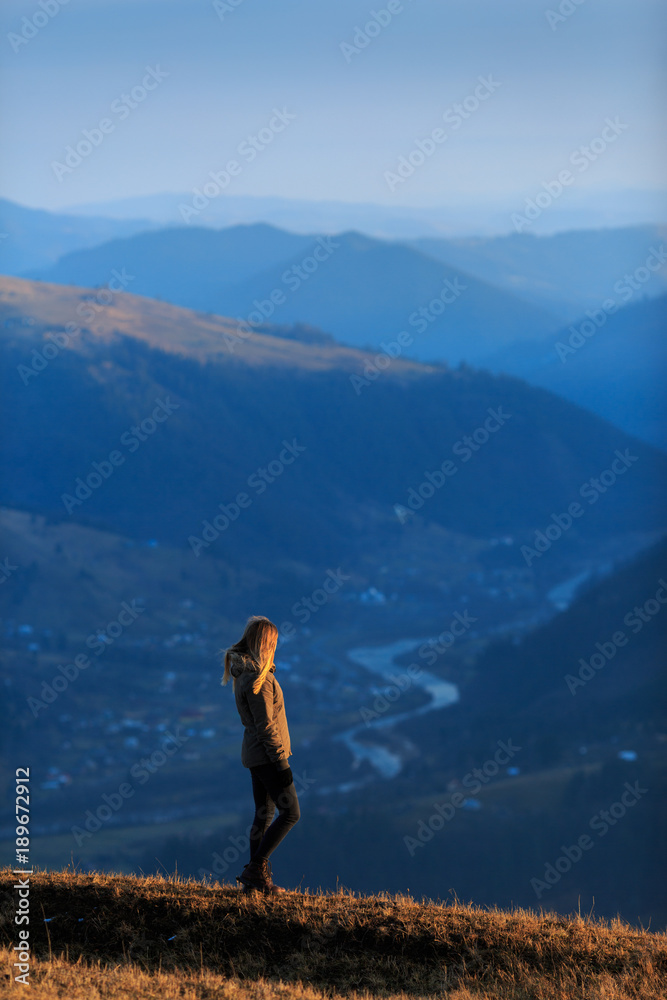 Naklejka premium Young woman hiker hiking on mountain trail. Travel concept. Happy traveler standing on top of a mountain and enjoying sunset view