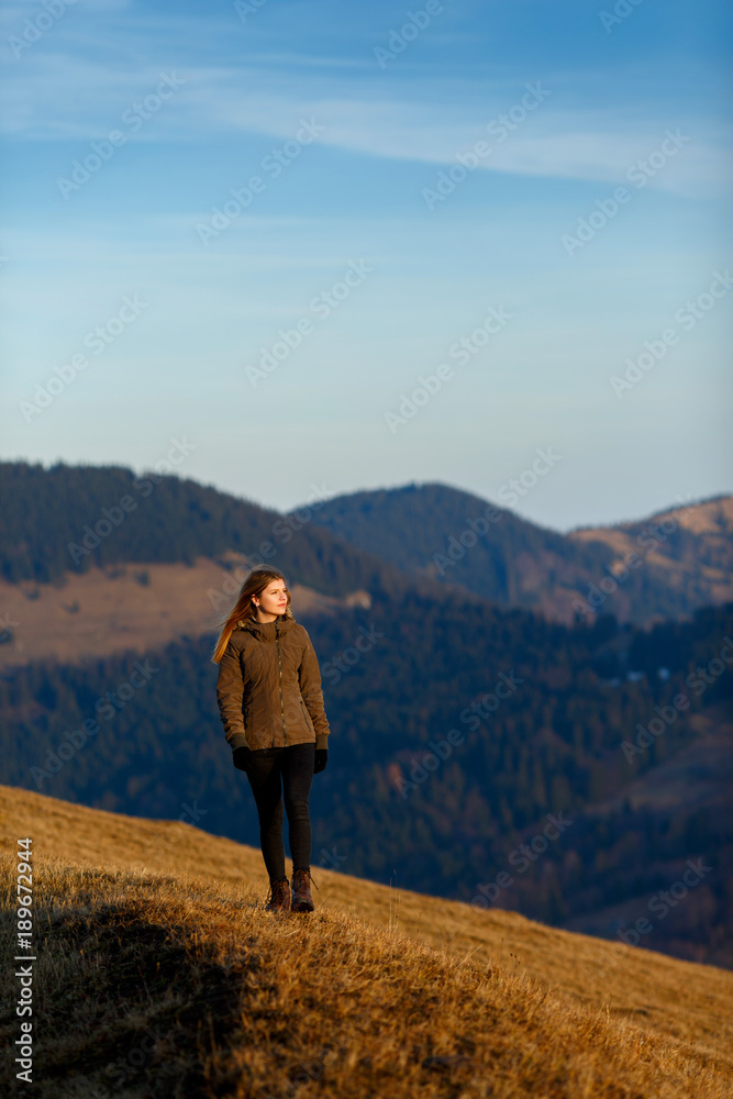 Young woman hiker hiking on mountain trail. Travel concept. Happy traveler standing on top of a mountain and enjoying sunset view