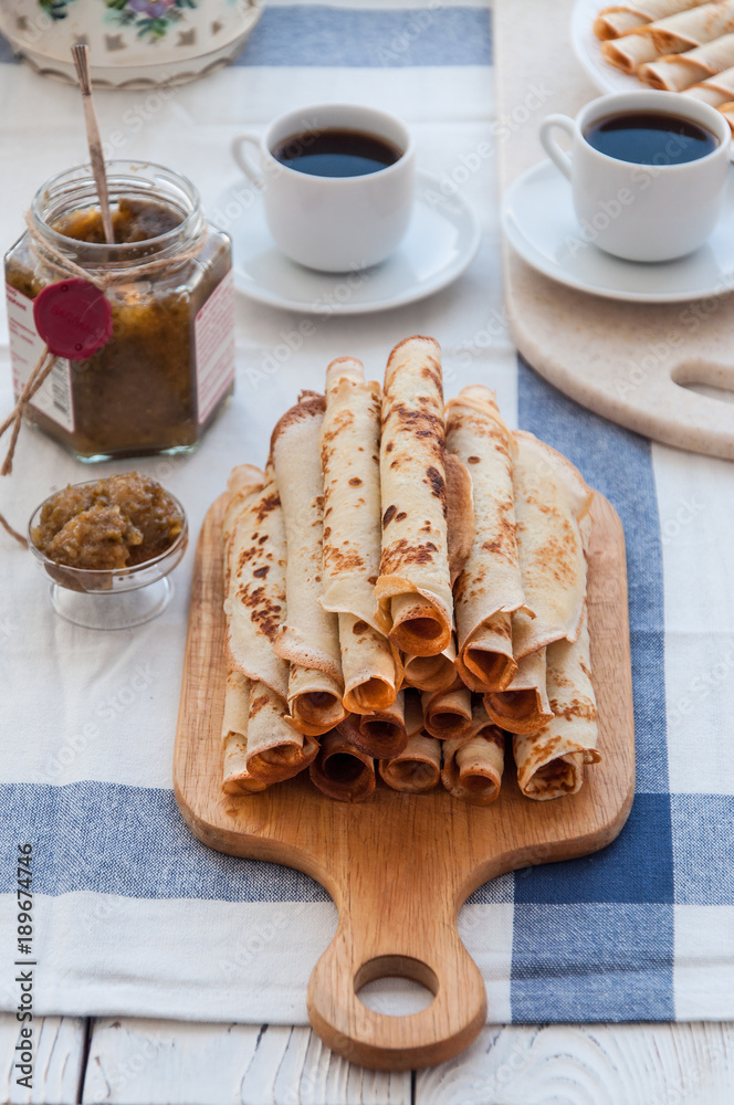 Fototapeta premium Thin pancakes for breakfast. Maslenitsa. On the table, a dish with pancakes, coffee and jam from feijoa