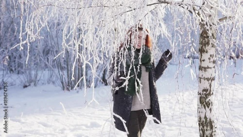 Young red-haired woman pushes a snow-covered branch and goes to the camera