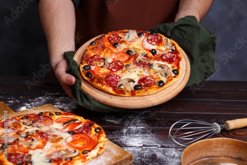 Chef baker with freshly baked delicious pizza in hands, close up. Pizza restaurant, cooking, kitchen concept