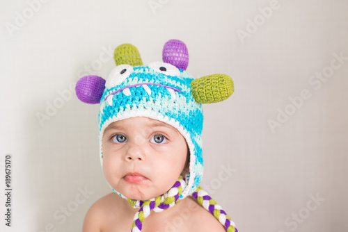 Blue-eyed baby boy on white background with little monster cap on head - Serious face