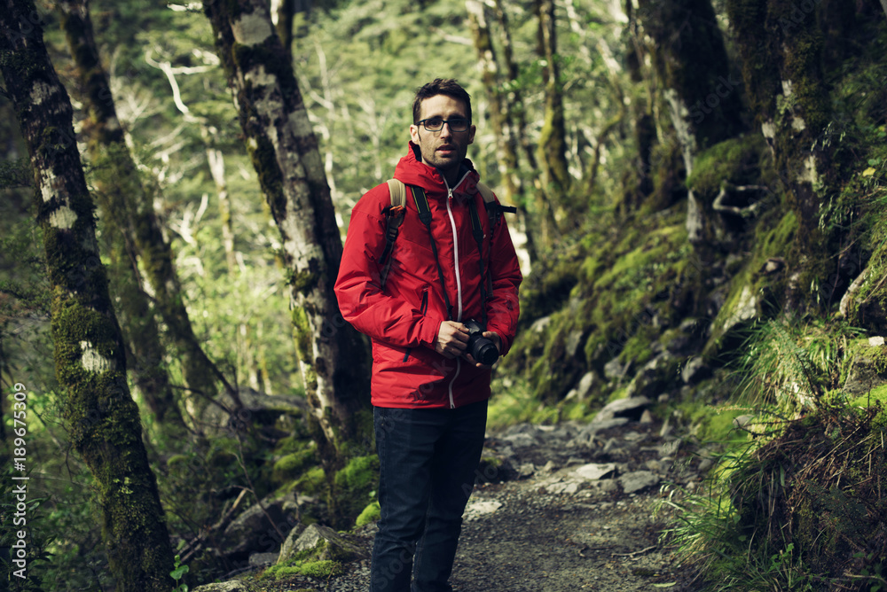 Retrato de hombre joven con gafas y chaquetón rojo con una cámara de fotos en medio del bosque. Retrato de hombre joven con gafas y chaquetón rojo con una cámara de fotos en medio del bosque.