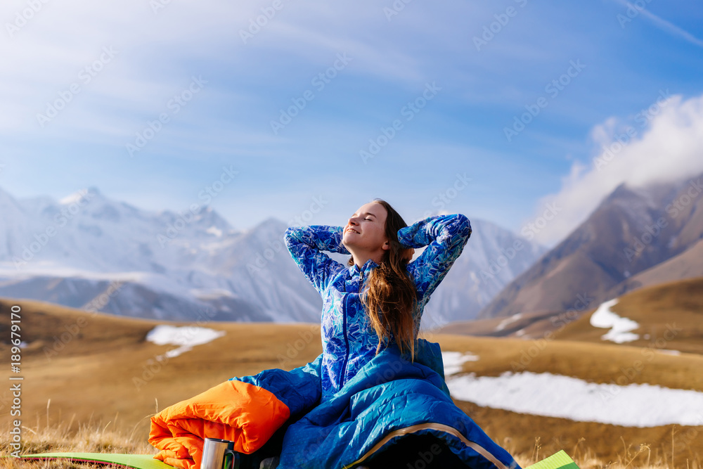 happy woman tourist sits on the background of mountains and pulls up