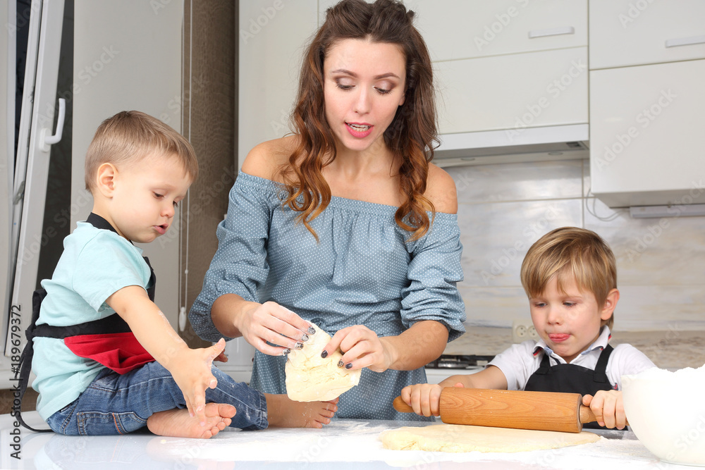 Fototapeta premium mom helps young sons knead the dough on the kitchen table
