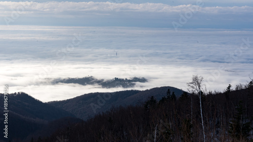 Landscape view from Sljeme or Medvednica mountain down on clouds covering the city of Zagreb in Croatia with a visible smoking heat plant chimney above the clouds during sunrise