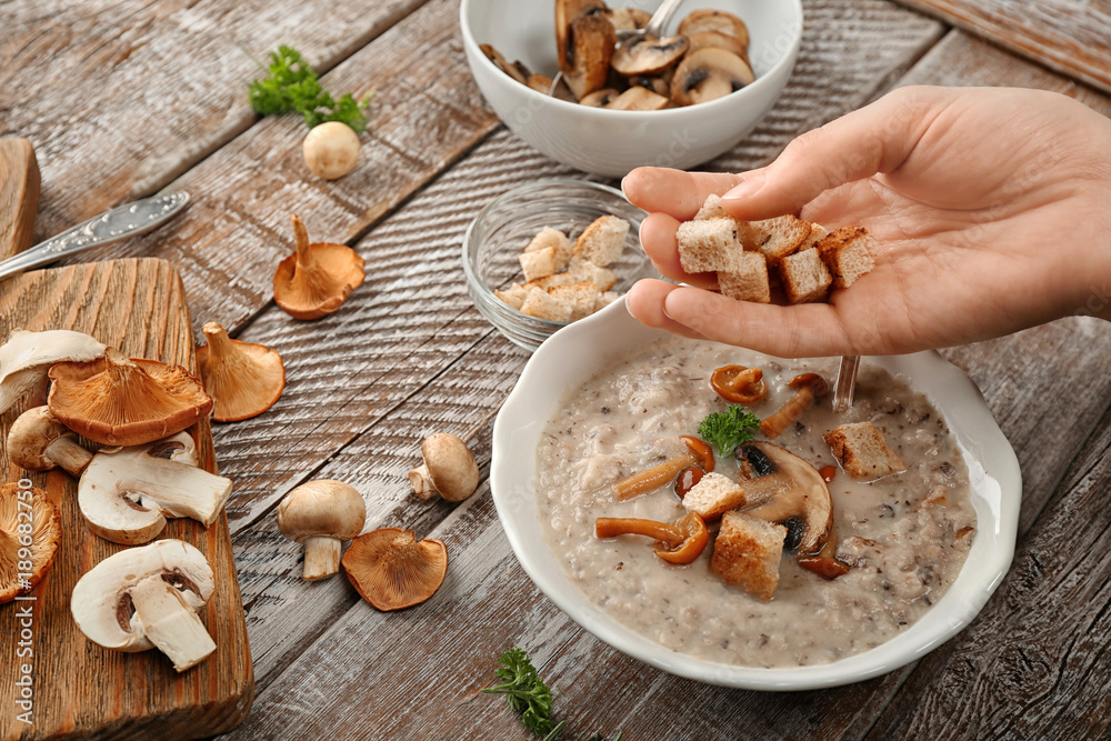 Young woman adding croutons to delicious mushroom soup at wooden table Young woman adding croutons to delicious mushroom soup at wooden table