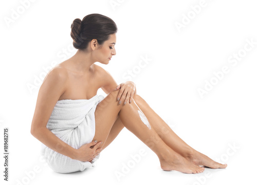 Young woman applying body cream on her leg against white background