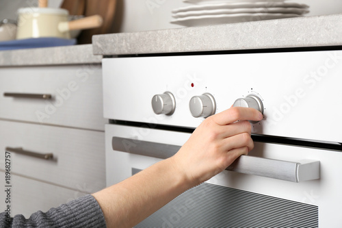 Young woman switching on modern electrical oven in kitchen