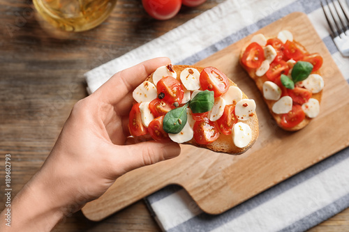 Woman holding tasty bruschetta with cherry tomatoes over table, closeup