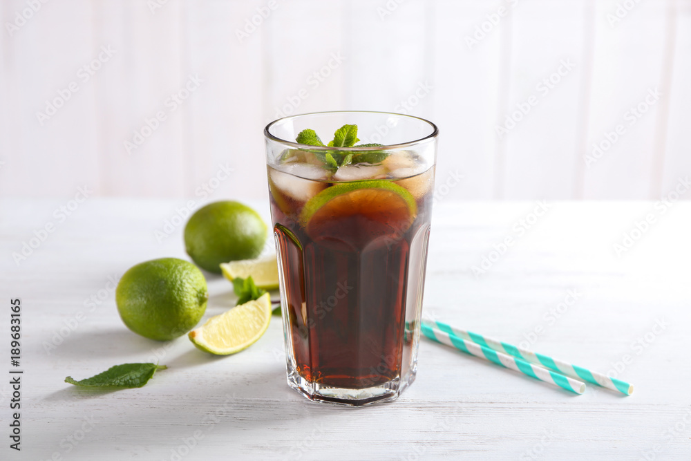 Glass of Cuba Libre cocktail on white wooden table Glass of Cuba Libre cocktail on white wooden table