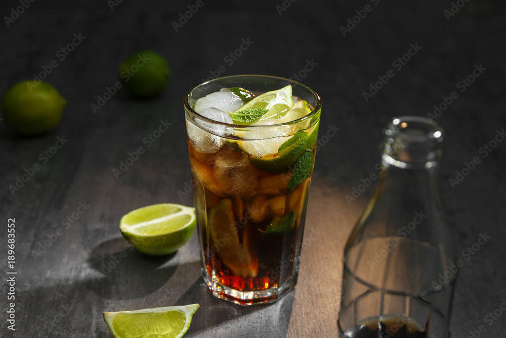 Glass with Cuba Libre cocktail and bottle of cola on table Glass with Cuba Libre cocktail and bottle of cola on table