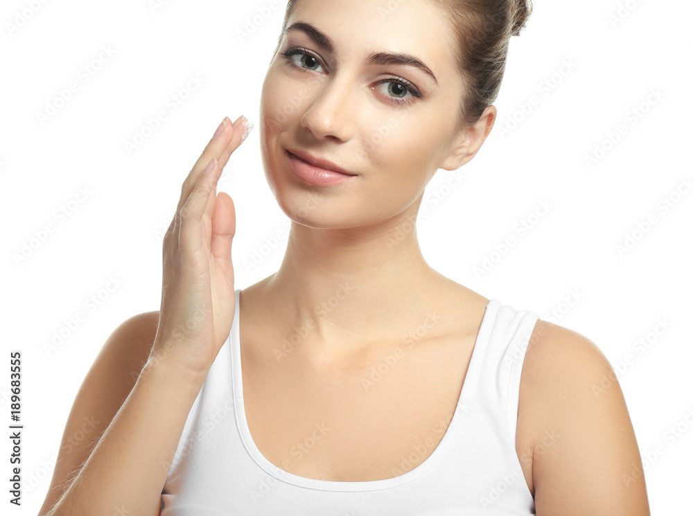 Beautiful young woman applying facial cream, on white background