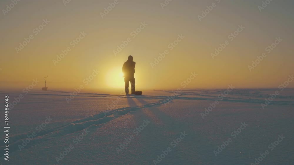 The fisherman is fishing on the background of a beautiful sunset. Winter fairy tale. Beautiful landscape The fisherman is fishing on the background of a beautiful sunset. Winter fairy tale. Beautiful landscape