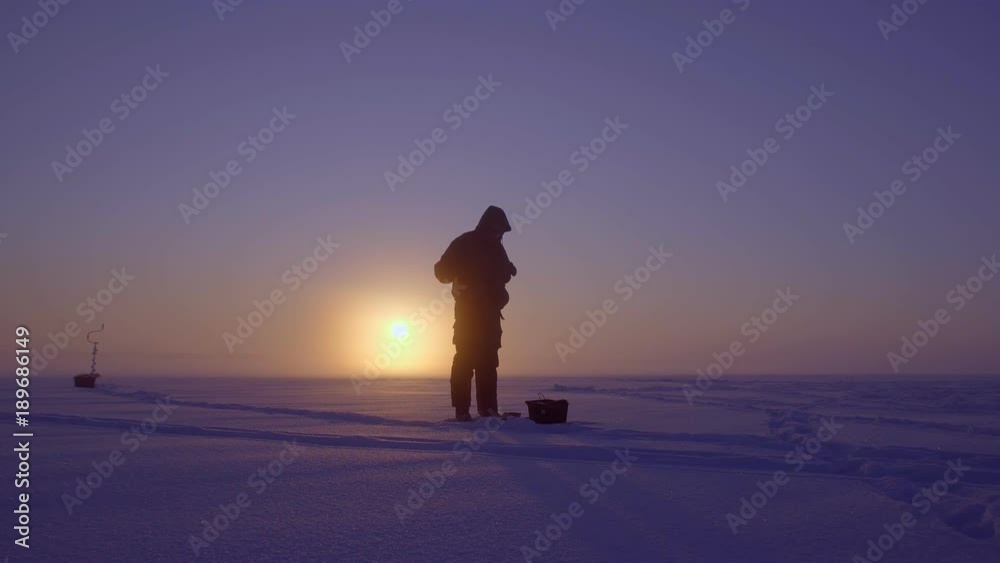The fisherman is fishing on the background of a beautiful sunset. Winter fairy tale. Beautiful landscape The fisherman is fishing on the background of a beautiful sunset. Winter fairy tale. Beautiful landscape
