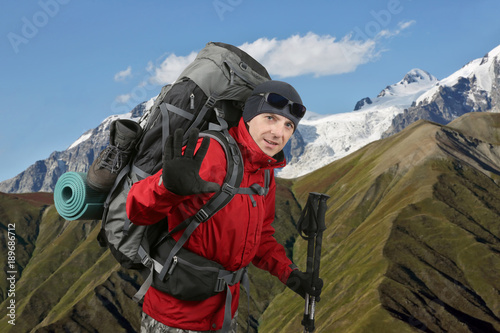 Happy traveler equipped with a red jacket on the hillside raised in greeting hand