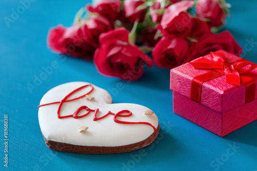 Fototapeta Naklejka Na Ścianę i Meble -  Gift box and bouquet of roses and gingerbread in the shape of heart with the inscription love for holiday on wooden background. Mother's Day, Happy birthday , Women's Day. St. Valentines Day