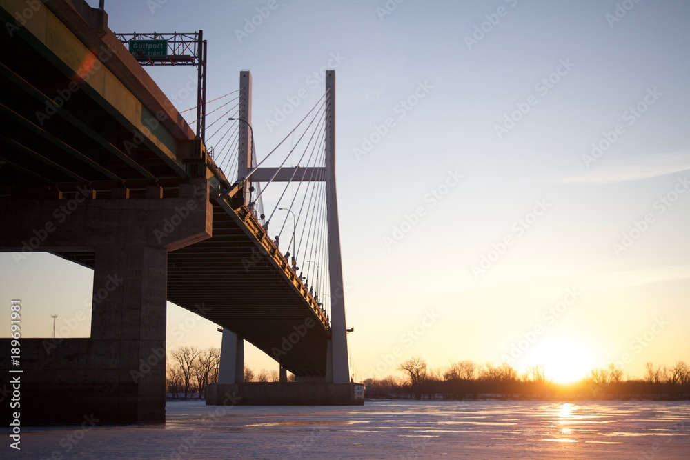 Fototapeta Sun rising besides a bridge over a frozen river