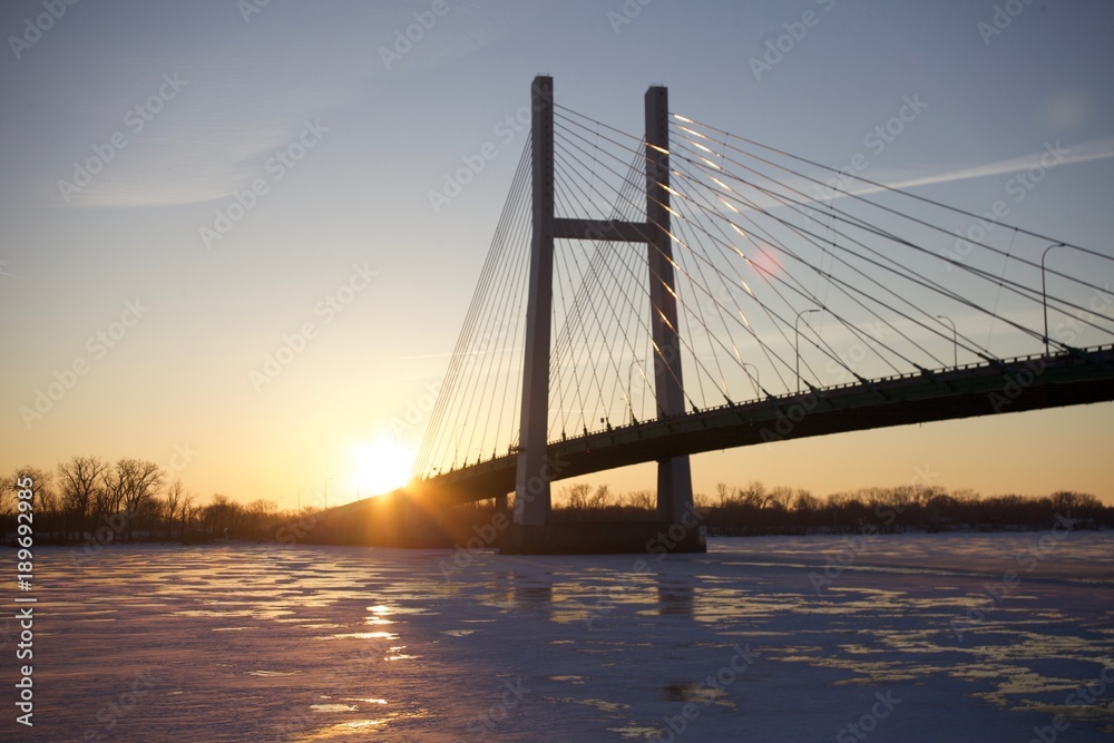 Fototapeta premium The sun reflecting off a bridge at sunrise over a river