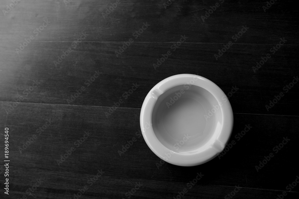black and white photo white ashtray on wood table with soft light upper right corner
