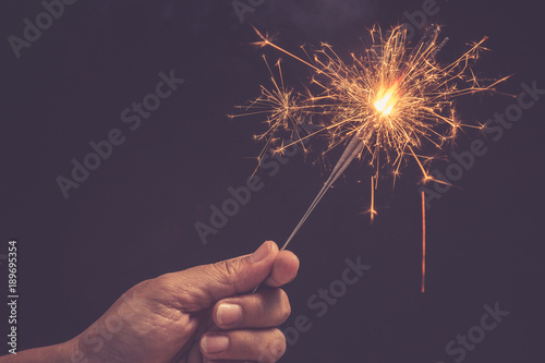 Christmas and new year celebration concept : Hand holding bright burning Christmas sparkle on black
