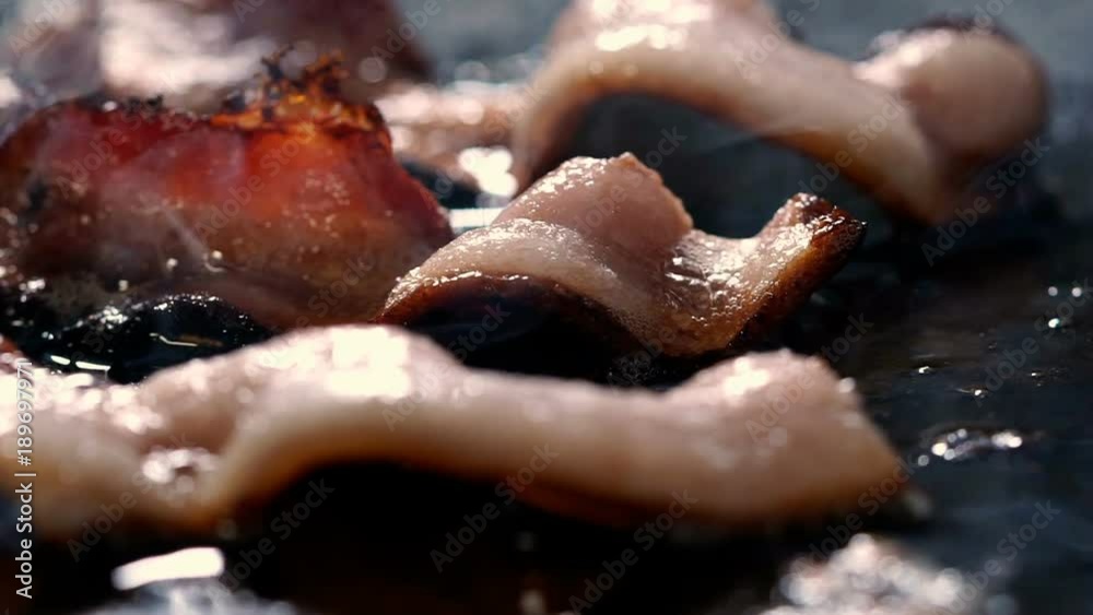 Bacon Frying - Slow motion macro panning video of pork bacon frying on black griddle. 