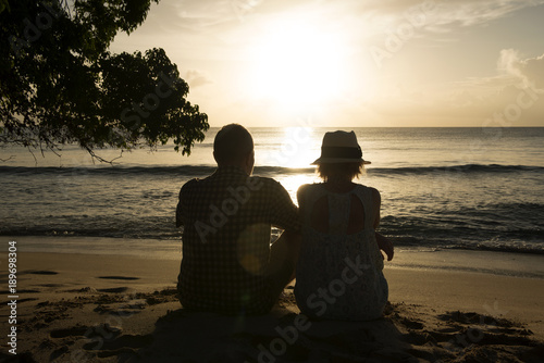 Couple Sitting on Sand and Looking to the Ocean and Sunset © photographyfirm