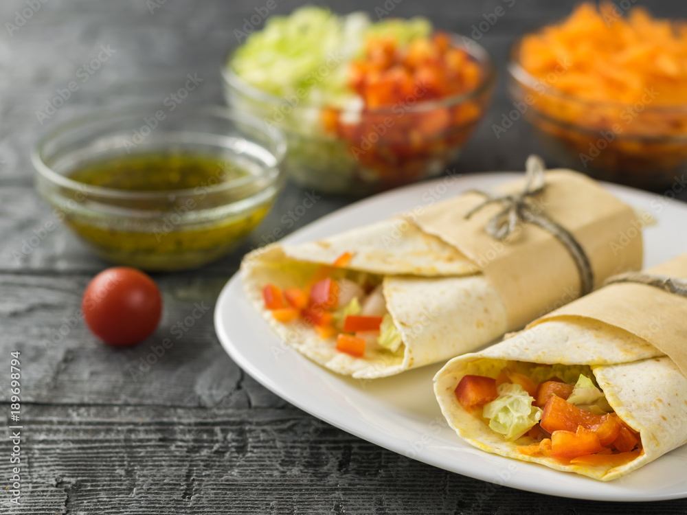 Two vegetable roll tortilla from wheat flour in white bowl on a wooden table with herbs. Two vegetable roll tortilla from wheat flour in white bowl on a wooden table with herbs.