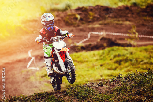 Racer child on motorcycle participates in motocross cross-country in flight, jumps and takes off on springboard against sky. Concept active extreme rest teenager.