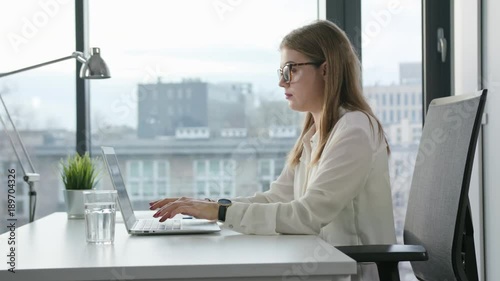 A young businesswoman sitting and using a laptop in the office. Medium. Dolly shot.