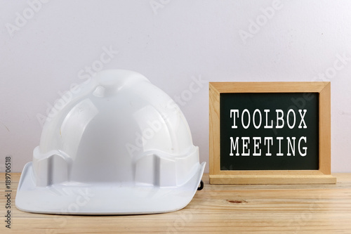 HEALTH AND SAFETY CONCEPT. Personal protective equipment on wooden table over white background with TOOLBOX MEETING text.