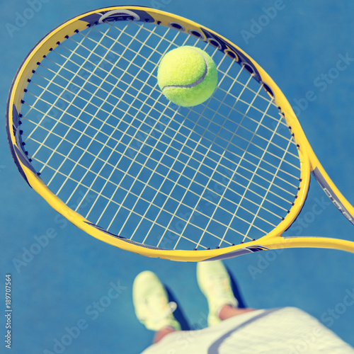 Tennis player girl taking pov selfie of racket and ball ready to play holding racket and showing shoes on blue outdoor tennis court. American hard court. © Maridav