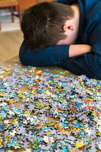 Tired teenager is sitting tilting his head next to puzzles