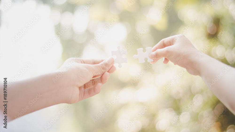 Man and woman hands connecting couple of puzzle with bokeh background.