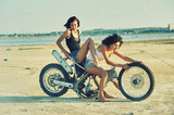 Two young women have fun playing on a disassembled motorcycle . Funny sexy girls