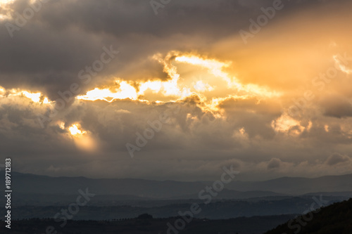 Sunset over a valley with sun rays coming out through some clouds