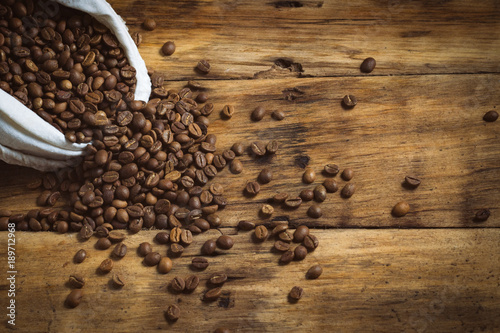 White bag with coffee beans are poured out on a wooden background. Copy space photo