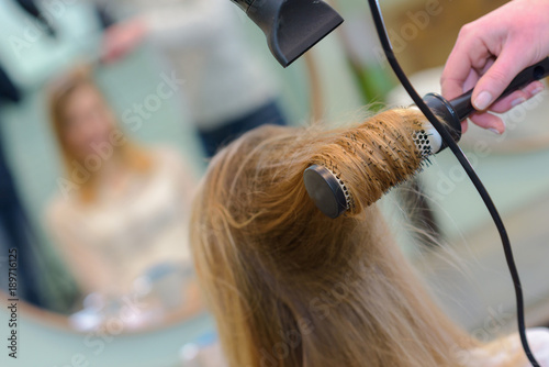 stylist drying hair of a female client at beauty salon