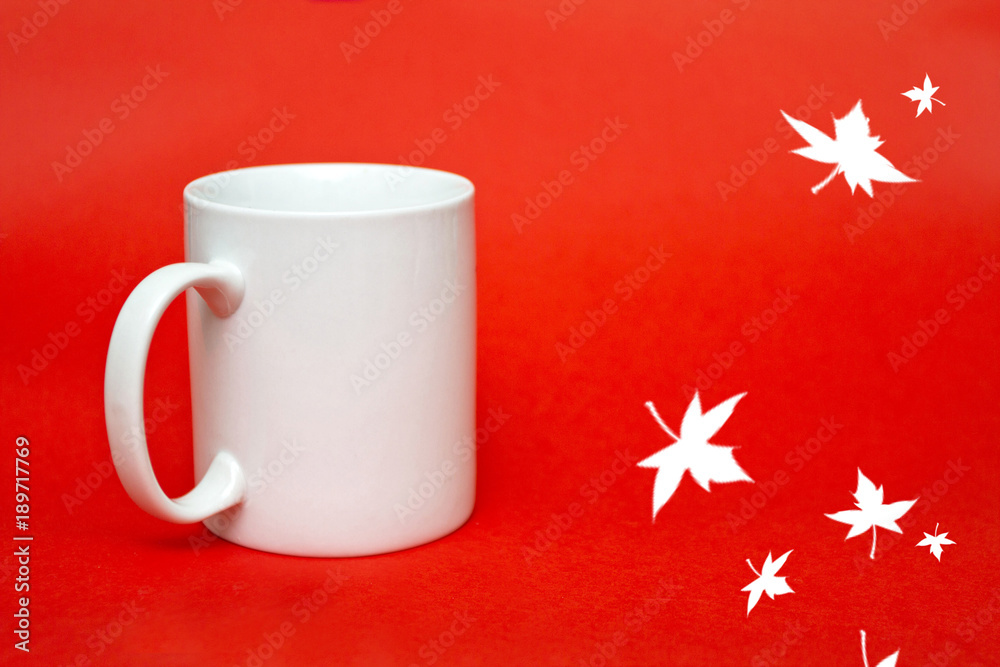 White mug on red background with leaves. Copy space for writing. White glass isolated. Holiday concept. Love concept. Gift and greeting card concept. Empty copy space White mug on red background with leaves. Copy space for writing. White glass isolated. Holiday concept. Love concept. Gift and greeting card concept. Empty copy space