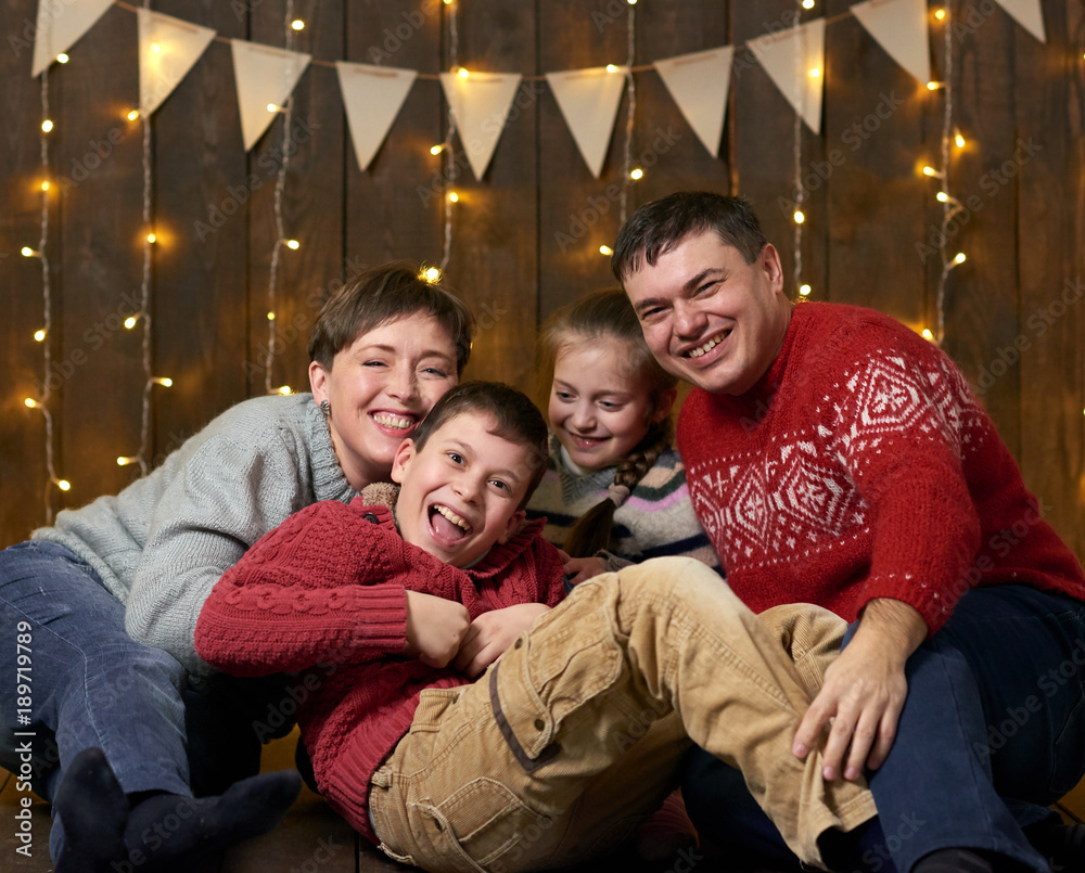 family sit together on wooden background with holiday lights and flags and having fun