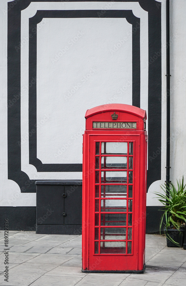 Fototapeta premium Red Telephone Box in front of a white wall in London at daylight.